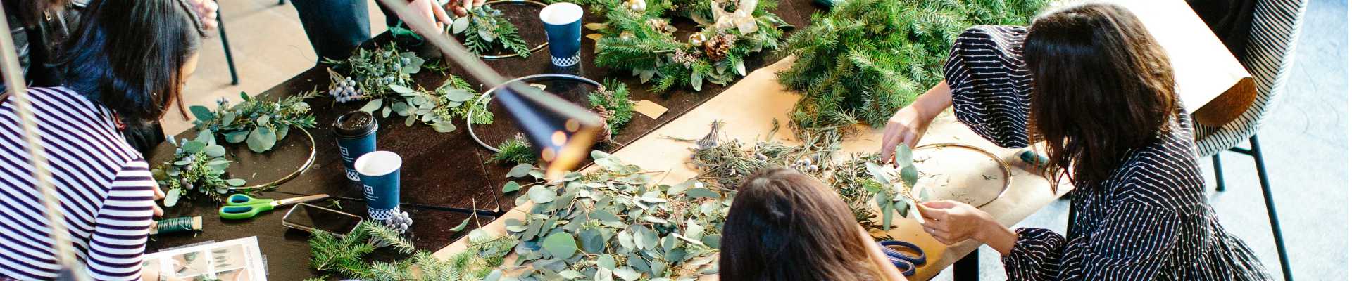 Mehrere Menschen basteln an einem Tisch Deko aus Tannezweigen.